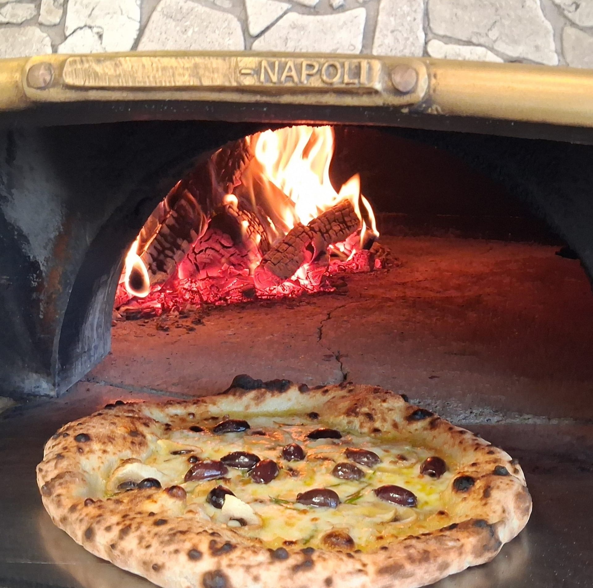 Mehevä pizza lähikuvassa etualalla ja taustalla tuli uunissa.  A juicy pizza in close-up in the foreground, with flames burning in the oven in the background.