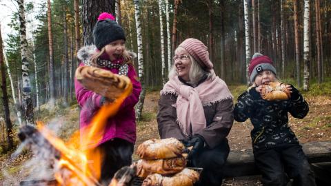 kuvassa lapset ja mummo paistamassa nuotiolla pullaa