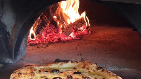 Mehevä pizza lähikuvassa etualalla ja taustalla tuli uunissa.  A juicy pizza in close-up in the foreground, with flames burning in the oven in the background.