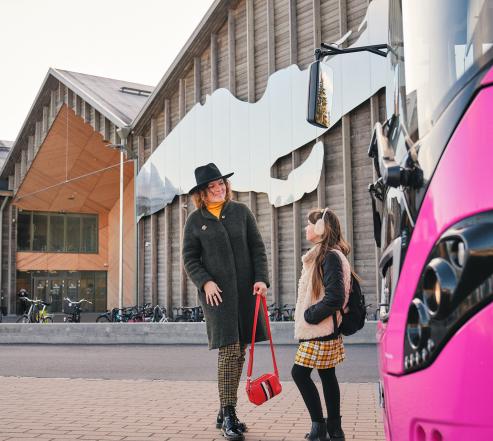 Kaksi henkilöä pinkin bussin edessä