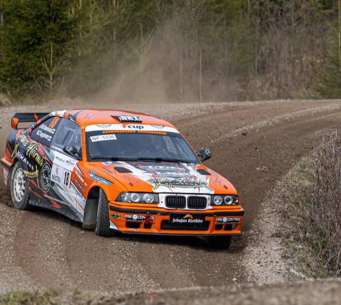 Oranssivalkoinen ralliauto ajaa hiekkatiellä lähikuvassa