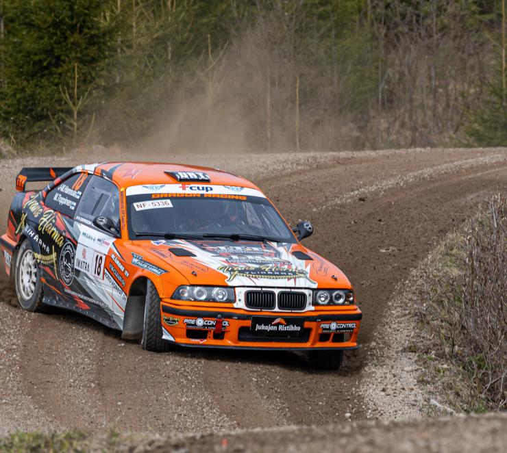 Oranssivalkoinen ralliauto ajaa hiekkatiellä lähikuvassa